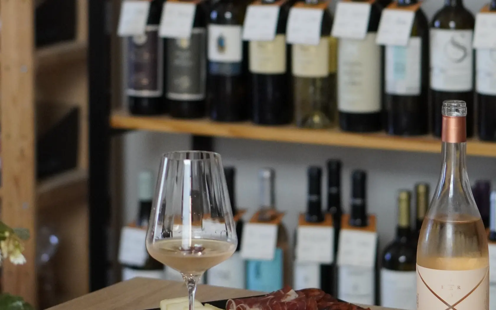 A glass of white wine and a petiscos board in front of the wine shelves at Aura Tavira